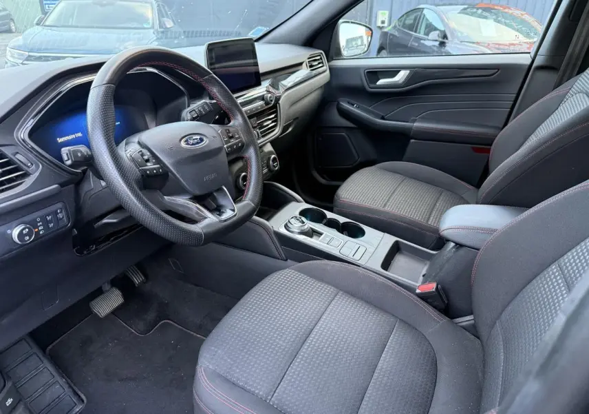 Intérieur avant du Ford Kuga 2022 gris, vue côté conducteur, volant ST-Line avec surpiqûres rouges et console centrale.