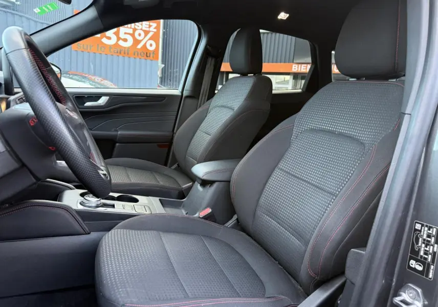 Vue intérieure côté conducteur du Ford Kuga 2022 avec sièges sport tissu noir et surpiqûres rouges ST-Line.