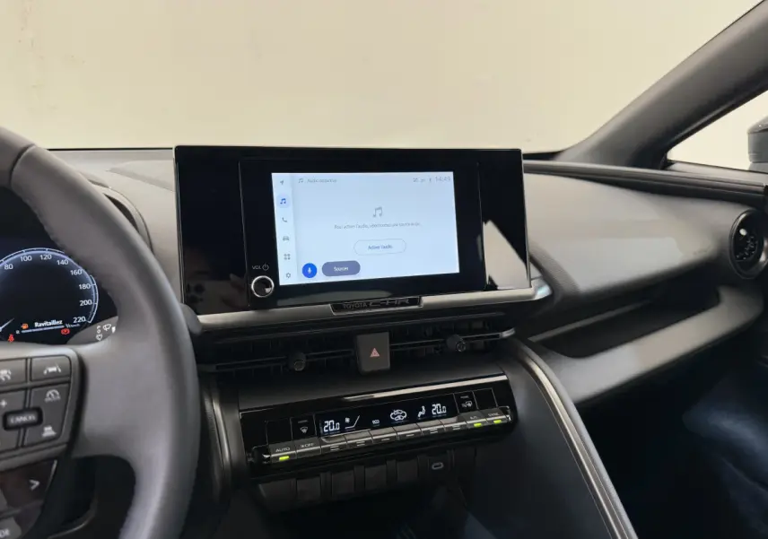 Vue intérieure du tableau de bord du Toyota C-HR 1.8 Hybride blanc, avec écran tactile central et commandes climatisation digitales.