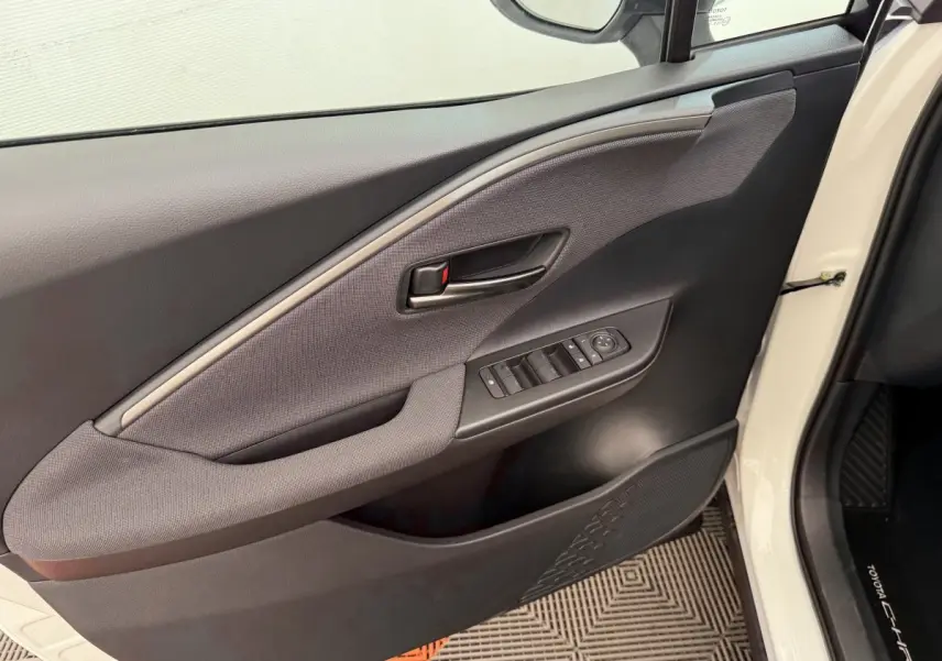 Vue rapprochée de la porte avant gauche blanche du Toyota C-HR 1.8 Hybride 140 Dynamic avec commandes de vitres et poignée noire.