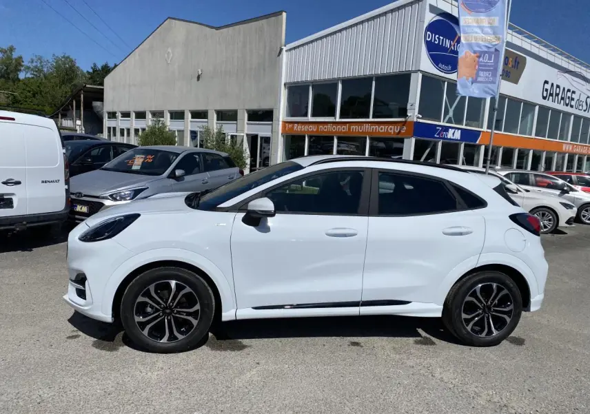 Vue de profil côté gauche d’un Ford Puma blanc Glacier avec jantes alliage noires et barres de toit noires, stationné en extérieur.