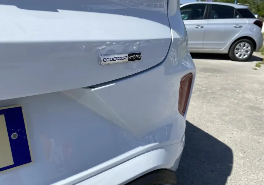 Gros plan sur l'arrière droit blanc glacier d'un Ford Puma avec badge EcoBoost Hybrid visible.