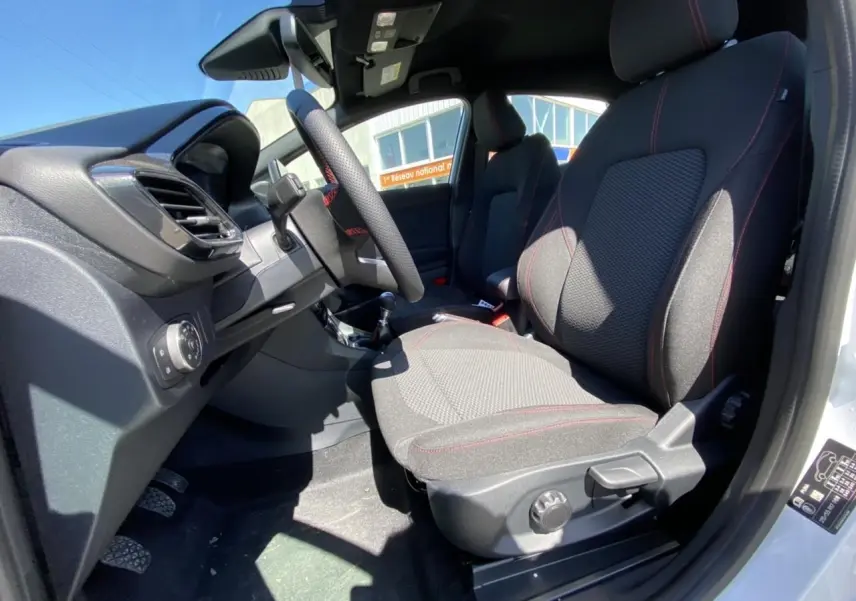 Vue intérieure côté conducteur du Ford Puma blanc glacier 2022, sièges tissu noir avec surpiqûres rouges et volant sport.