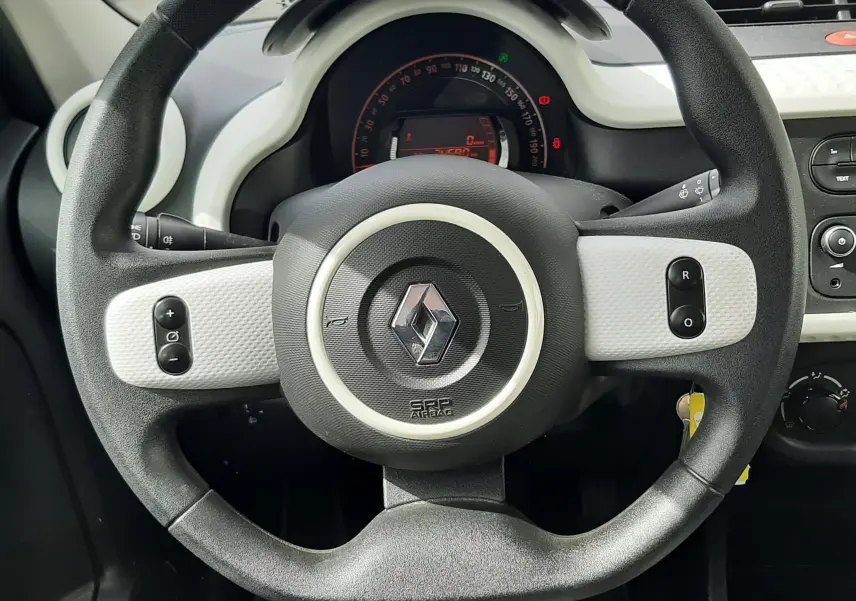 Vue intérieure du tableau de bord et volant de la Renault Twingo III blanche, avec levier de vitesse manuel et commandes centrales visibles.