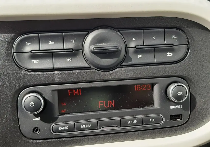 Vue rapprochée des commandes de climatisation noires sur tableau de bord gris d'une Renault Twingo III blanche.