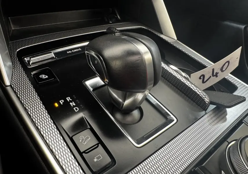 Gros plan sur la console centrale noire du Mazda CX-60 2024, avec levier de vitesse automatique et molette de sélection.