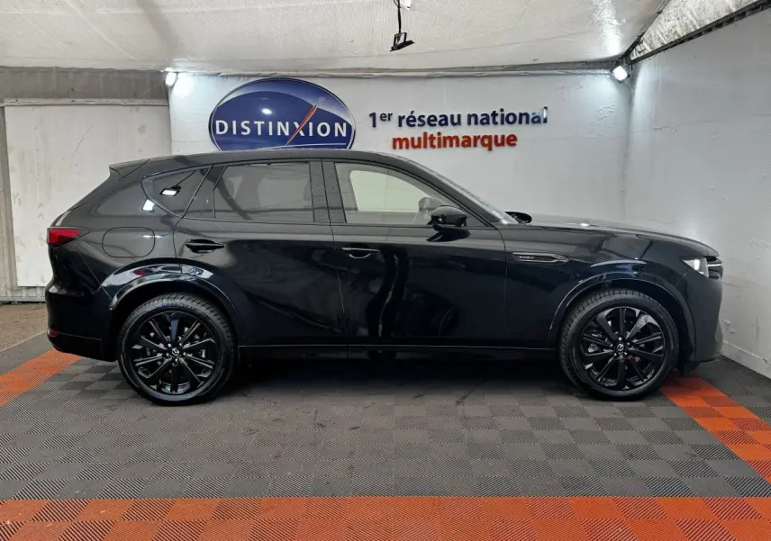 Vue de profil côté gauche du SUV Mazda CX-60 noir brillant avec jantes noires dans un garage éclairé.