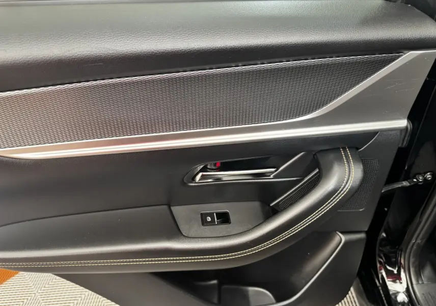 Vue intérieure côté gauche de la porte avant noire du Mazda CX-60 avec poignée chromée et surpiqûres beiges.