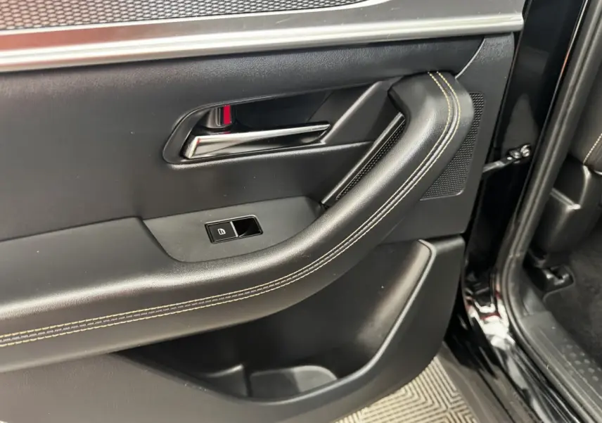 Vue rapprochée de la porte arrière droite noire du Mazda CX-60 2024, avec poignée intérieure et couture beige visible.