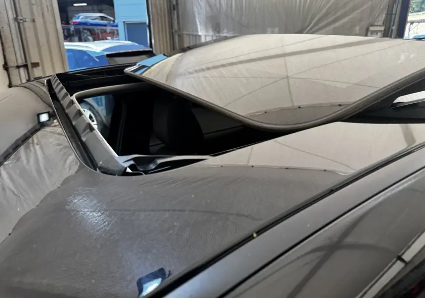 Toit ouvrant panoramique ouvert sur le côté gauche d'un Mazda CX-60 noir, vue rapprochée en intérieur d'atelier.