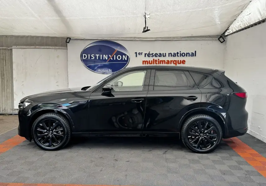 Vue latérale droite du Mazda CX-60 noir 2024 avec jantes noires et vitres teintées dans un showroom.