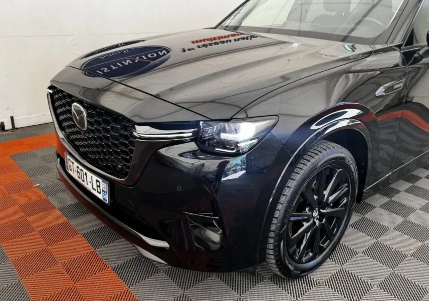 Vue 3/4 avant droit du Mazda CX-60 noir brillant avec calandre imposante et phares LED allumés.