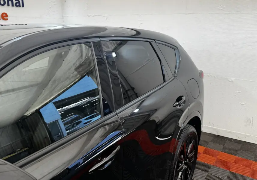 Vue latérale droite du Mazda CX-60 noir 2024 avec jantes noires et vitres teintées dans un garage.