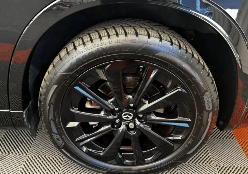 Gros plan sur la roue avant droite noire du Mazda CX-60 2024 avec jante alliage brillante et logo Mazda central.