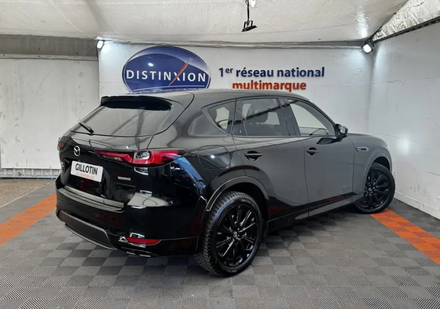 Vue 3/4 arrière droite d'un Mazda CX-60 noir brillant avec jantes noires dans un showroom.