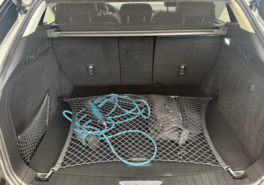 Coffre ouvert vu de l'arrière d'un Mazda CX-60 noir 2024 avec câble de recharge bleu retenu par filet.