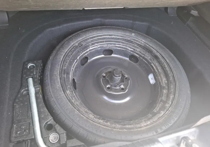 Gros plan sur la roue de secours noire et les outils dans le coffre d’une Volkswagen Golf gris clair 2023.
