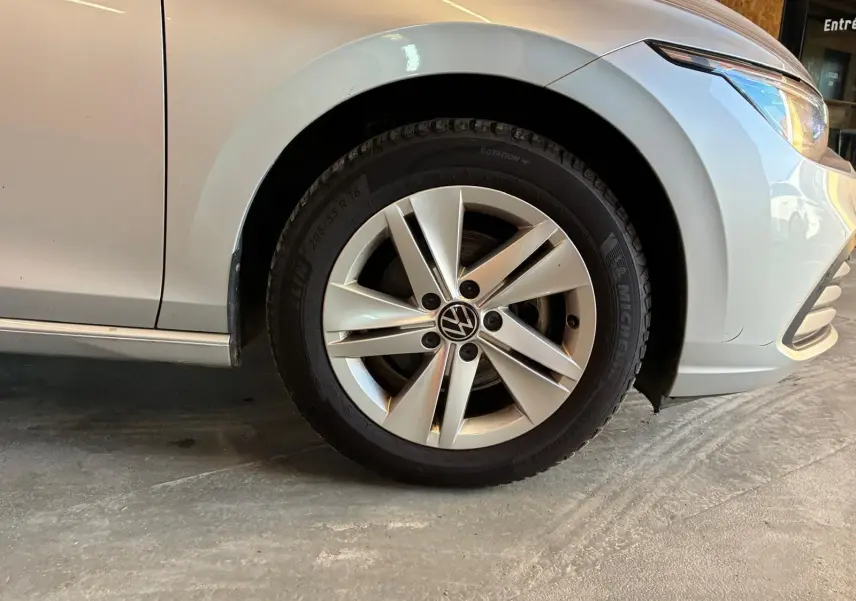 Gros plan sur la roue avant droite d'une Volkswagen Golf gris clair 2023, avec jante alliage et partie avant visible.