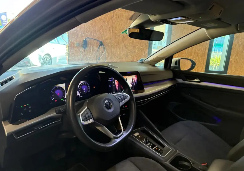 Vue intérieure côté conducteur de la Volkswagen Golf gris clair 2023, avec tableau de bord numérique et écran tactile central.
