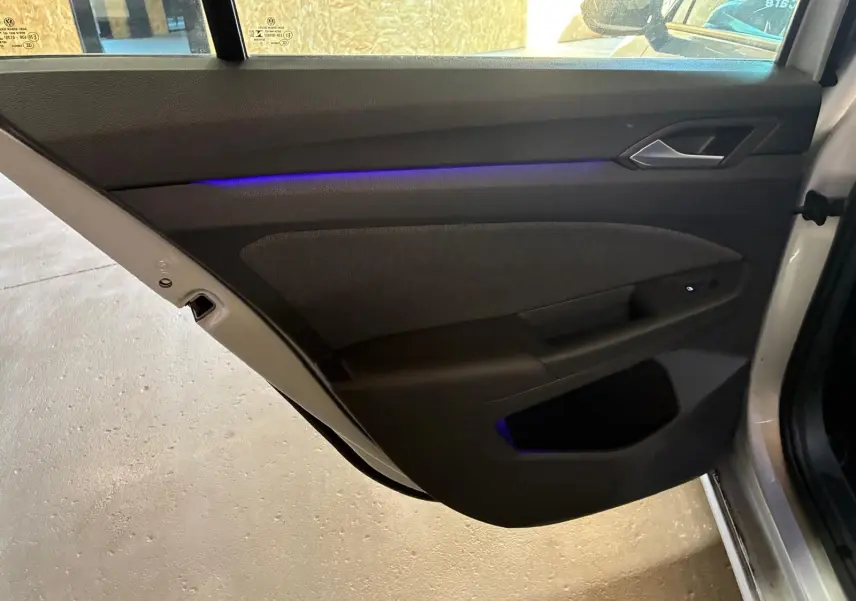 Vue intérieure de la porte arrière droite d'une Volkswagen Golf gris clair 2023 avec éclairage d'ambiance bleu.