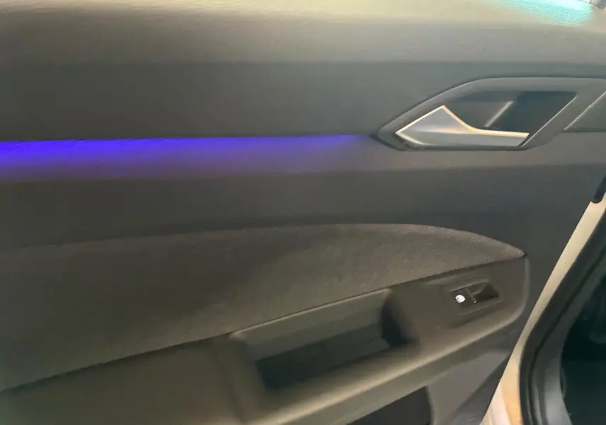 Détail de la porte intérieure côté conducteur de la Volkswagen Golf gris clair 2023 avec éclairage d’ambiance bleu.