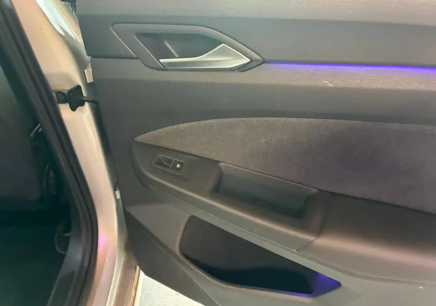 Gros plan sur la porte intérieure côté gauche d'une Volkswagen Golf gris clair avec éclairage d'ambiance violet.