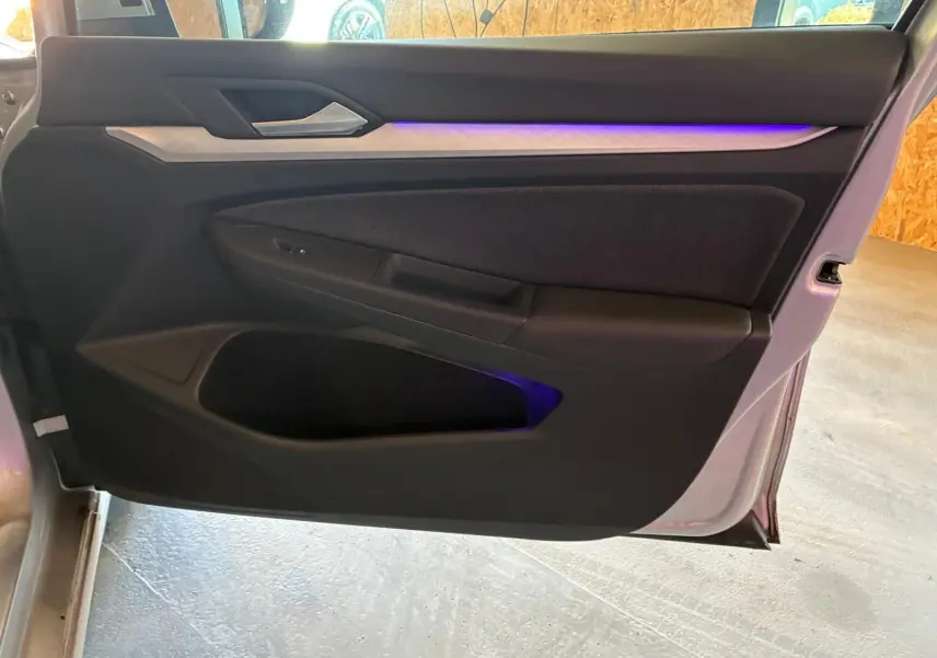 Vue intérieure de la porte avant gauche d'une Volkswagen Golf gris clair 2023 avec éclairage d'ambiance violet.