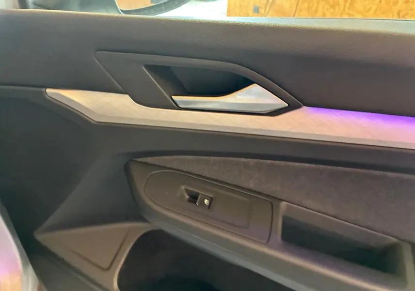 Détail de la porte côté gauche de la Volkswagen Golf 2023, avec insert décoratif clair et éclairage d'ambiance violet.