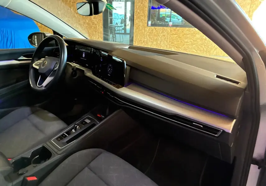 Vue intérieure côté conducteur de la Volkswagen Golf 2023 gris clair, avec tableau de bord digital et éclairage d'ambiance violet.