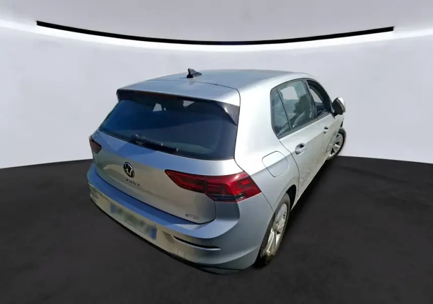 Vue 3/4 arrière droite d'une Volkswagen Golf gris clair 2023, avec feux arrière LED et logo VW visible sur le hayon.