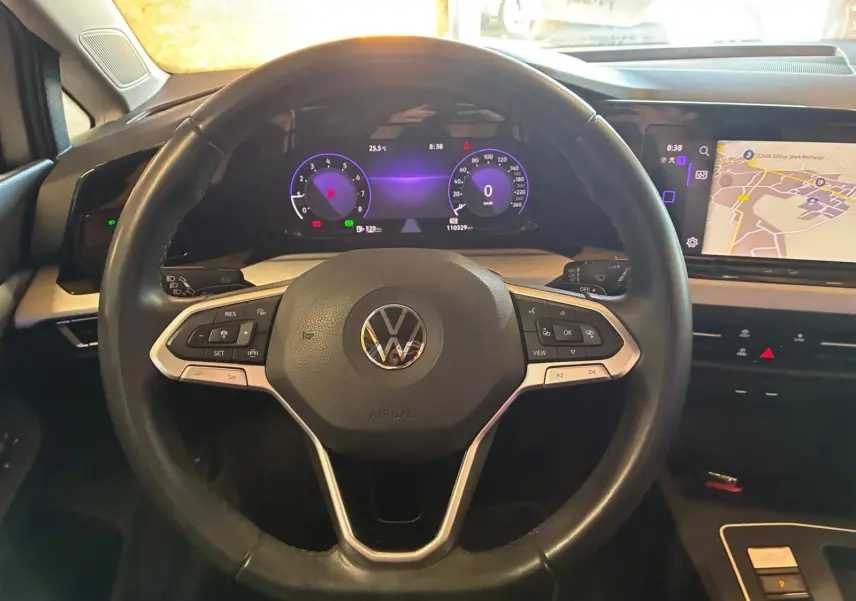Vue intérieure centrée sur le volant noir de la Volkswagen Golf 2023 avec tableau de bord numérique et écran de navigation.