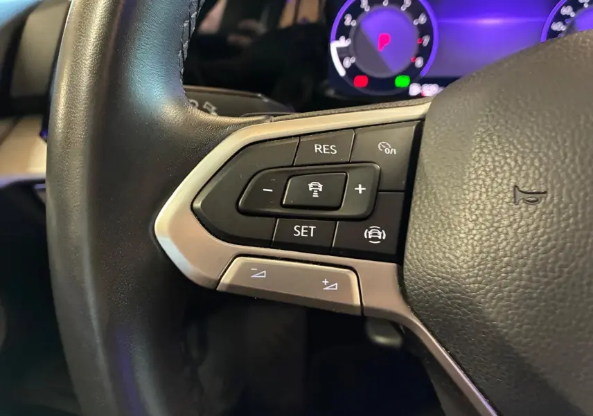 Gros plan sur les commandes au volant gauche de la Volkswagen Golf gris clair 2023, avec affichage numérique en arrière-plan.