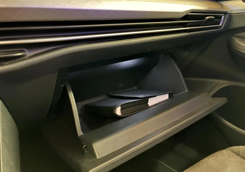 Gros plan sur la boîte à gants ouverte de la Volkswagen Golf gris clair 2023, avec un carnet noir à l'intérieur.