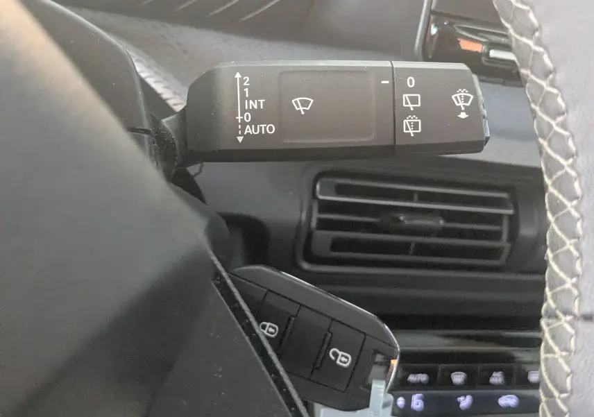 Gros plan sur la manette d’essuie-glace noire à gauche du volant dans l’habitacle gris noir du Citroën E-C3 2025.