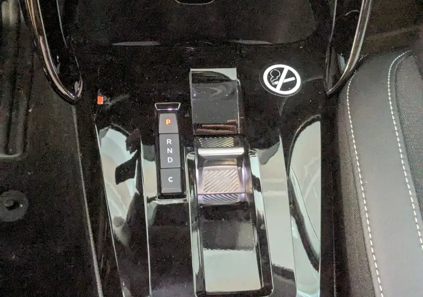 Gros plan sur la console centrale noire brillante de la Citroën E-C3 113 MAX avec sélecteur de boîte automatique et symbole interdiction de fumer.