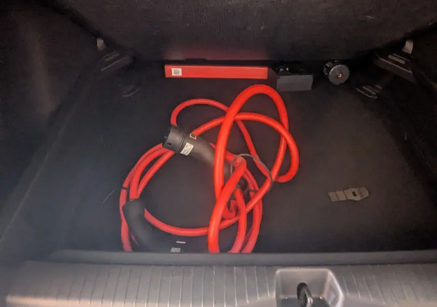 Vue intérieure du coffre d'une Citroën E-C3 113 MAX noir 2025, avec câble de recharge électrique rouge enroulé.