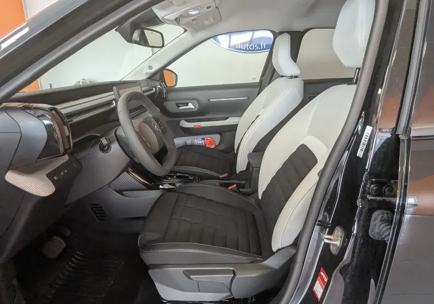 Vue intérieure côté conducteur de la Citroën E-C3 113 MAX 2025 noire, sièges tissu bicolore noir et gris clair.