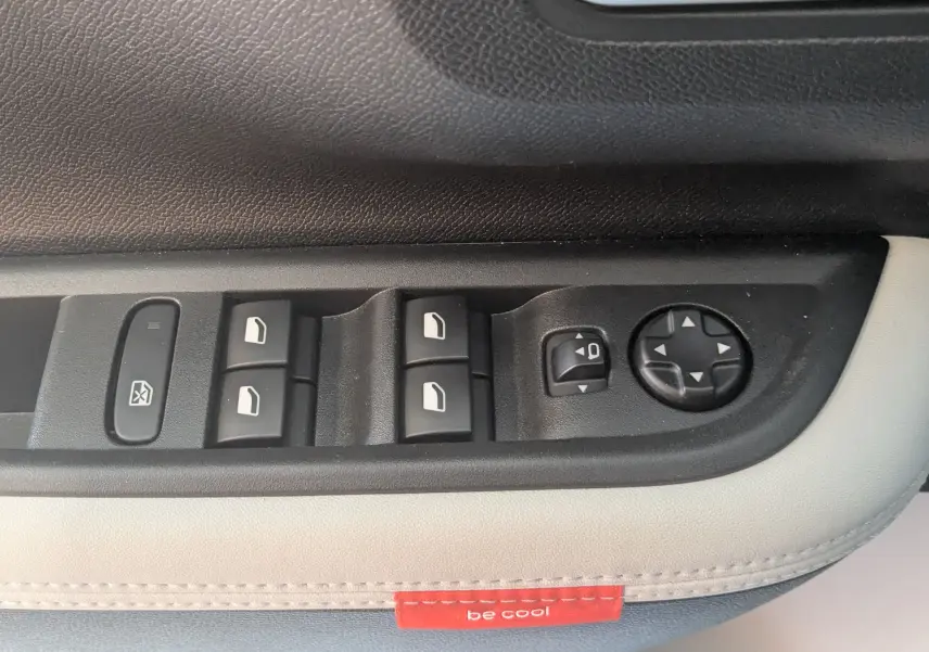 Gros plan sur les commandes de vitres et rétroviseurs côté conducteur de la Citroën E-C3 113 MAX 2025, sellerie gris noir.