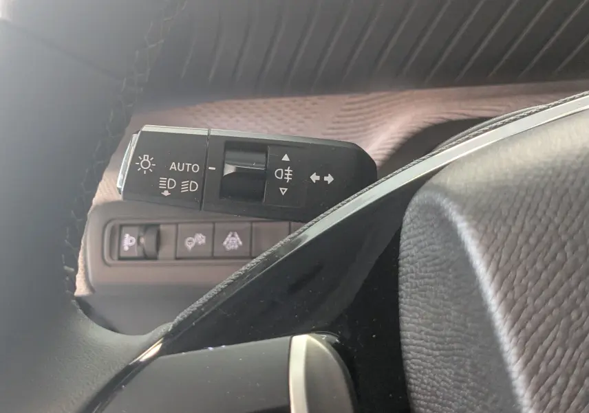 Gros plan sur la commande des feux et clignotants à gauche du volant dans l’habitacle gris noir du Citroën E-C3 2025.