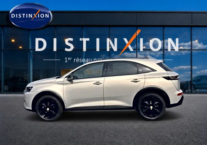 Vue de profil côté gauche du DS7 1.5 BlueHDi 130 Crystal Pearl avec jantes noires devant une vitrine Distinxion.