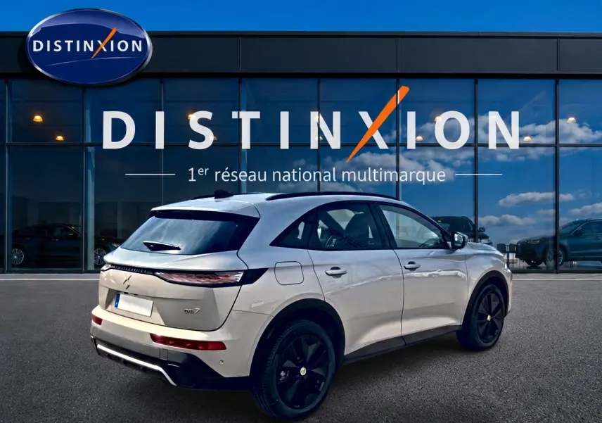 Vue 3/4 arrière droite d'un DS7 Crystal pearl garé devant une vitrine avec logo Distinxion en arrière-plan.