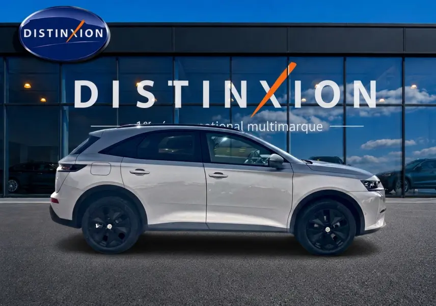 Vue latérale droite du DS7 1.5 BlueHDi 130 Crystal Pearl avec jantes noires devant une vitrine Distinxion.