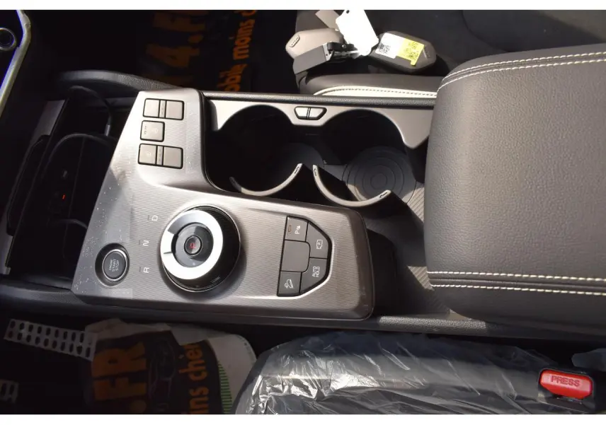 Vue rapprochée de la console centrale grise du Kia Sportage hybride 2026 avec sélecteur rotatif et accoudoir cuir noir.