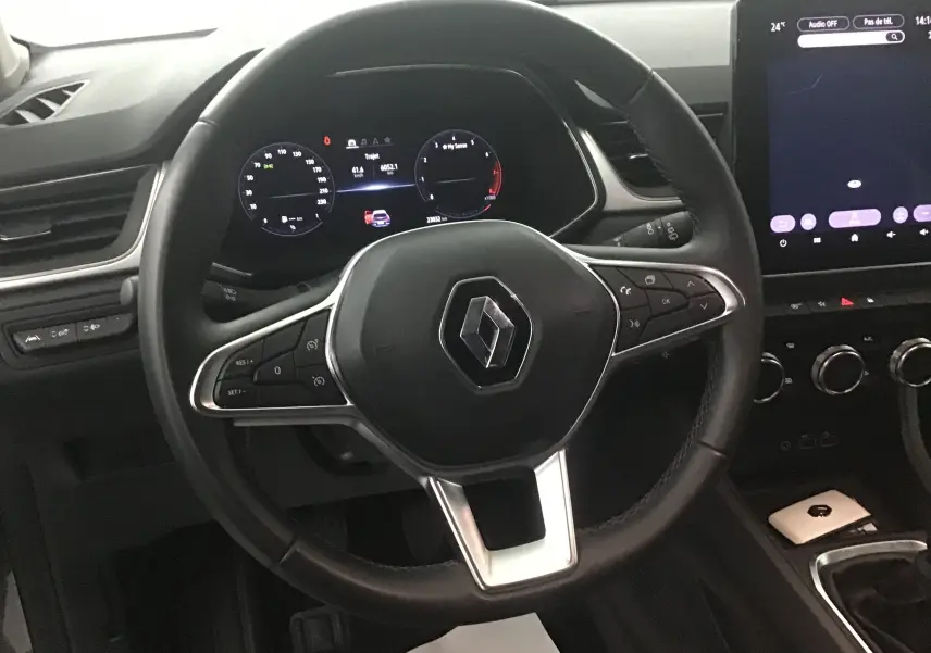 Vue rapprochée du volant noir du Renault Captur 2024 avec tableau de bord digital et écran tactile central allumé.