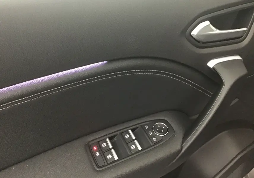 Gros plan sur la porte côté gauche du Renault Captur 2024 gris Cassiopée/Noir avec commandes électriques et éclairage d'ambiance violet.