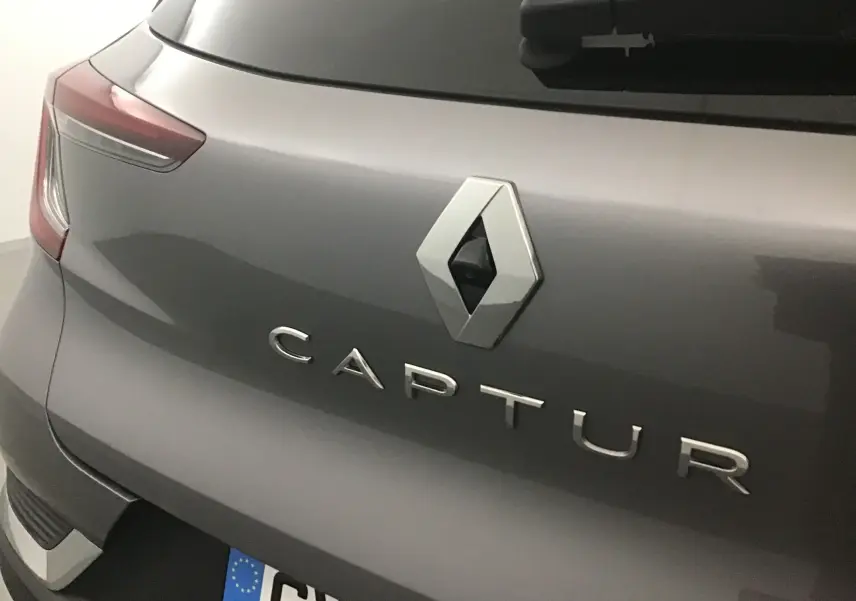 Gros plan sur l'arrière gris cassiopée du Renault Captur 2024, mettant en valeur le logo et la caméra de recul intégrée.