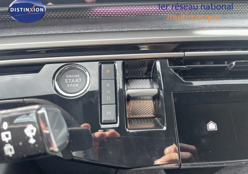 Gros plan sur la console centrale noire brillante du Peugeot 5008 Hybrid 2025 avec bouton start et commandes de boîte automatique.