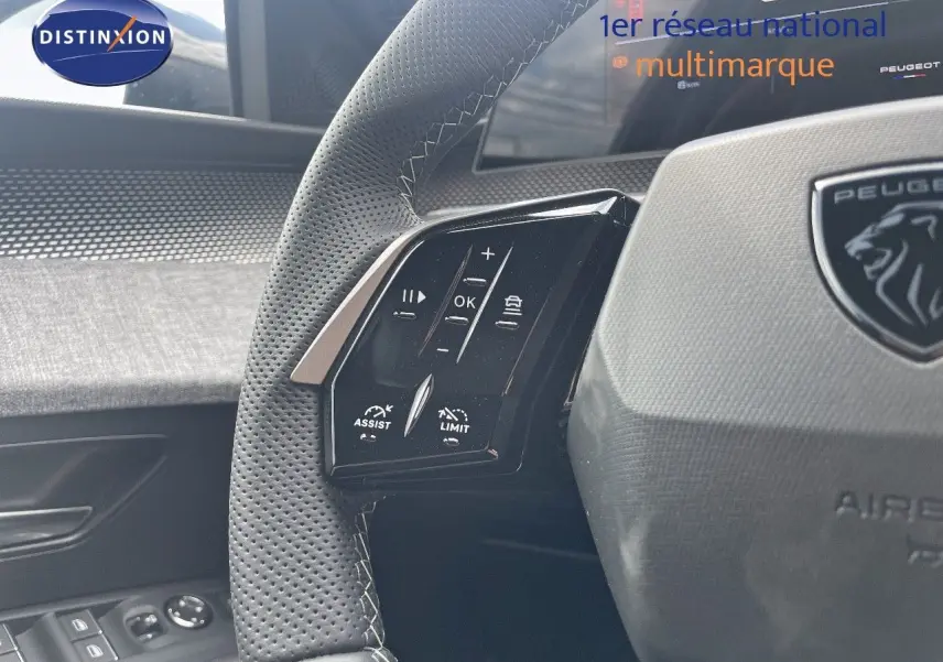 Gros plan sur le volant en cuir perforé avec commandes intégrées du Peugeot 5008 Hybrid 2025, intérieur noir et gris.
