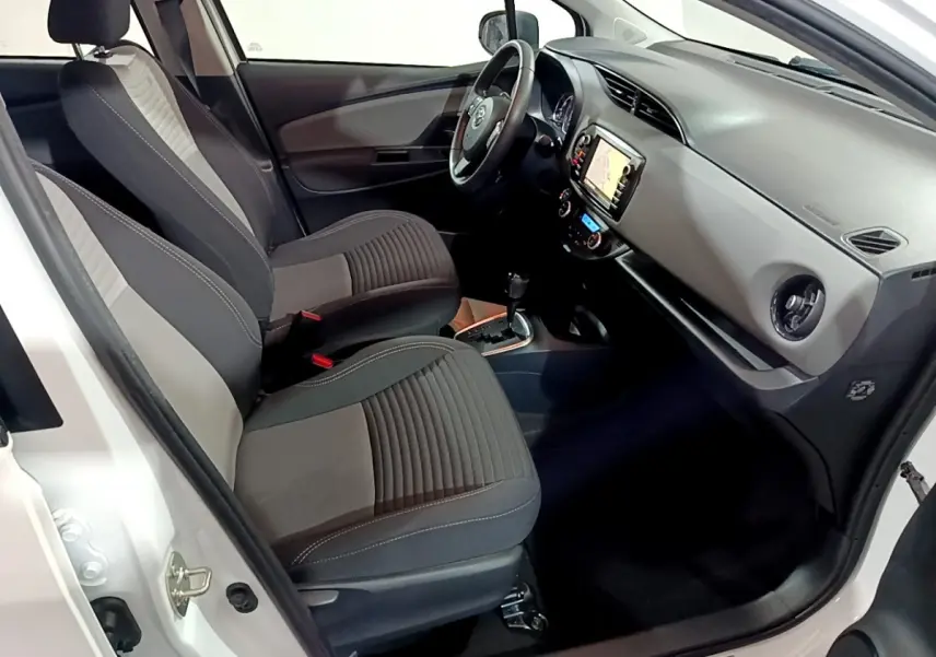Intérieur avant droit de la Toyota Yaris blanche 2020, sièges bi-ton gris, volant cuir alu et écran tactile navigation.