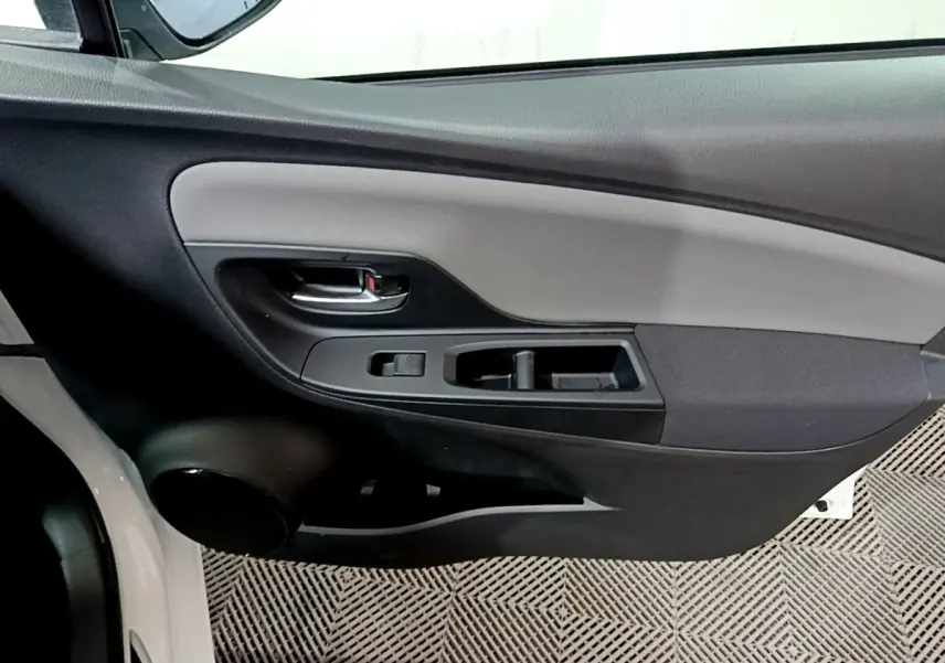 Vue intérieure du panneau de porte avant gauche de la Toyota Yaris blanche, avec commandes de vitres et poignée noire.